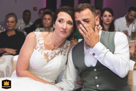At Château des Selves in Seillans, France, the bride and groom are seated and emotional, wiping tears as they are moved by a surprise slideshow.